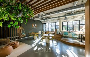 Lichte kantoorruimte met houten details en planten aan het plafond, gelegen op Westblaak 180 in Rotterdam Centrum, ideaal voor wie een kantoor wil huren. Verschillende zitopties beschikbaar.