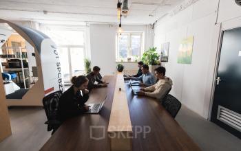 Gezellig kantoorpand Schiedamse Vest 154 in Rotterdam Centrum met meerdere mensen aan lange tafels die werken op laptops.