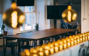 Kantoorruimte huren op Schiedamse Vest 154, Rotterdam Centrum. Grote tafel met zwarte stoelen, hanglampen, en een flatscreen tv in een goed verlichte ruimte.