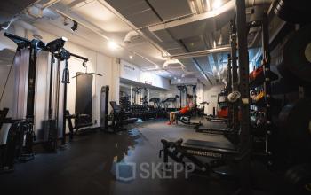 Kantoorruimte huren op Schiedamse Vest 154, Rotterdam Centrum, moderne fitnessruimte met diverse fitnessapparaten en gewichten, man bezig met krachttraining.