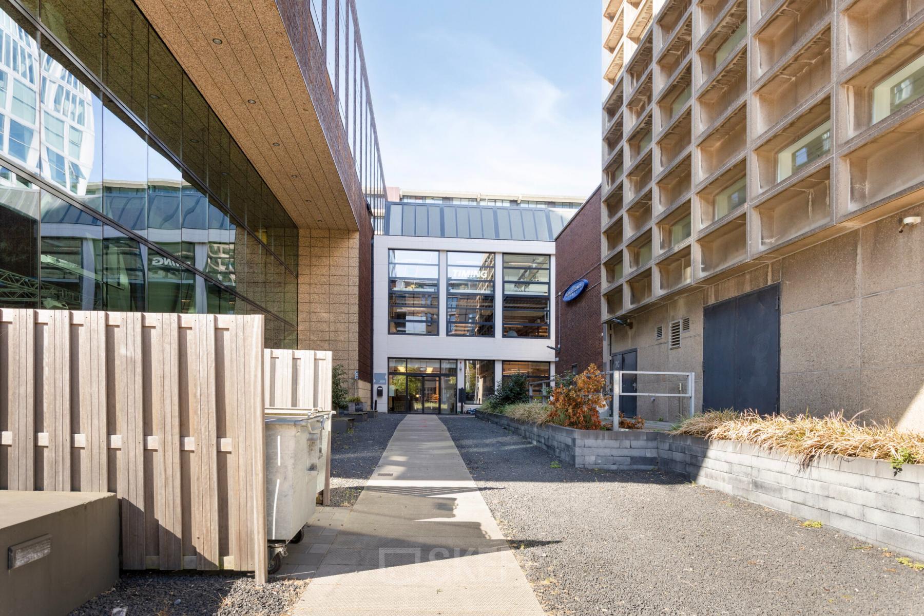 Het exterieur van een modern kantoorpand op Lloydstraat 21 B in Rotterdam Delfshaven, met een open binnenplaats en toegangspad, ideaal voor wie kantoorruimte wil huren.