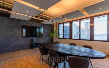 Moderne vergaderruimte in een kantoorpand aan de Kratonkade 7-27 in Rotterdam Delfshaven, met uitzicht op de skyline. Voorzien van een grote ovale tafel en stoelen.