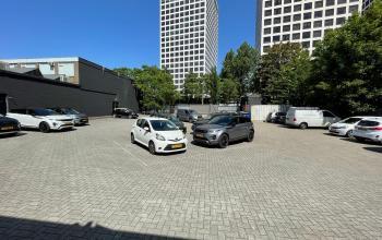 Parkeerplaats naast kantoorpand op Van Helmontstraat 17-23 in Rotterdam Delfshaven, met geparkeerde auto's en omringende hoge gebouwen.