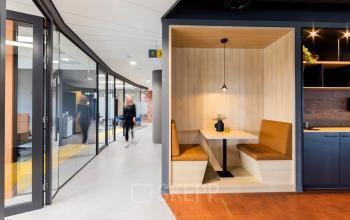 Interieur van kantoorpand op Wilhelminaplein 1-40 in Rotterdam Kop van Zuid. Moderne inrichting met houten zitplek en passerende medewerkers in een lichte gang. Ideale locatie om kantoorruimte te huren.