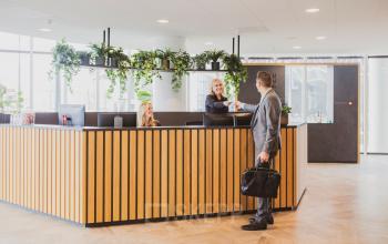 Zakelijke lobby op Wilhelminaplein 1-40, Rotterdam met twee mensen bij de receptie, omringd door groene planten. Ideaal om kantoorruimte te huren in een moderne omgeving.