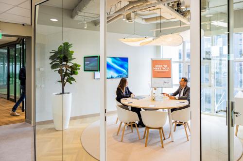 Moderne en lichte vergaderruimte in kantoorpand Wilhelminaplein 1-40, Rotterdam Kop van Zuid, met mensen die in gesprek zijn rond een ronde tafel. Geschikt voor kantoorruimte huren.