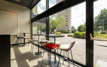 Modern kantoorpand in Rotterdam Kralingen met hoge ramen, kleurrijke stoelen aan bartafels en uitzicht op groen.