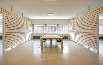 Ruime kantoorpand op Linker Rottekade 292 in Rotterdam Noord, met grote houten tafel omringd door stoelen, ideaal voor vergaderingen of samenwerkingsprojecten. Huur deze lichte ruimte voor een functionele werkplek.