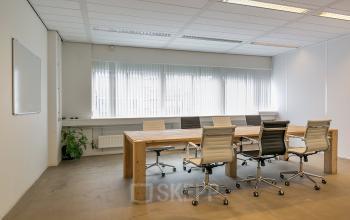 Moderne vergaderruimte in kantoorpand aan de Linker Rottekade 292 in Rotterdam Noord, met een grote houten tafel en comfortabele stoelen, ideaal voor vergaderingen. Veel natuurlijk licht door grote ramen.