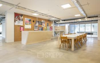 Moderne kantoorruimte huren in Rotterdam Noord met ruime tafel en houten stoelen, naast een stijlvolle bar. Ideaal voor creatieve vergaderingen of workshops in een inspirerende omgeving.