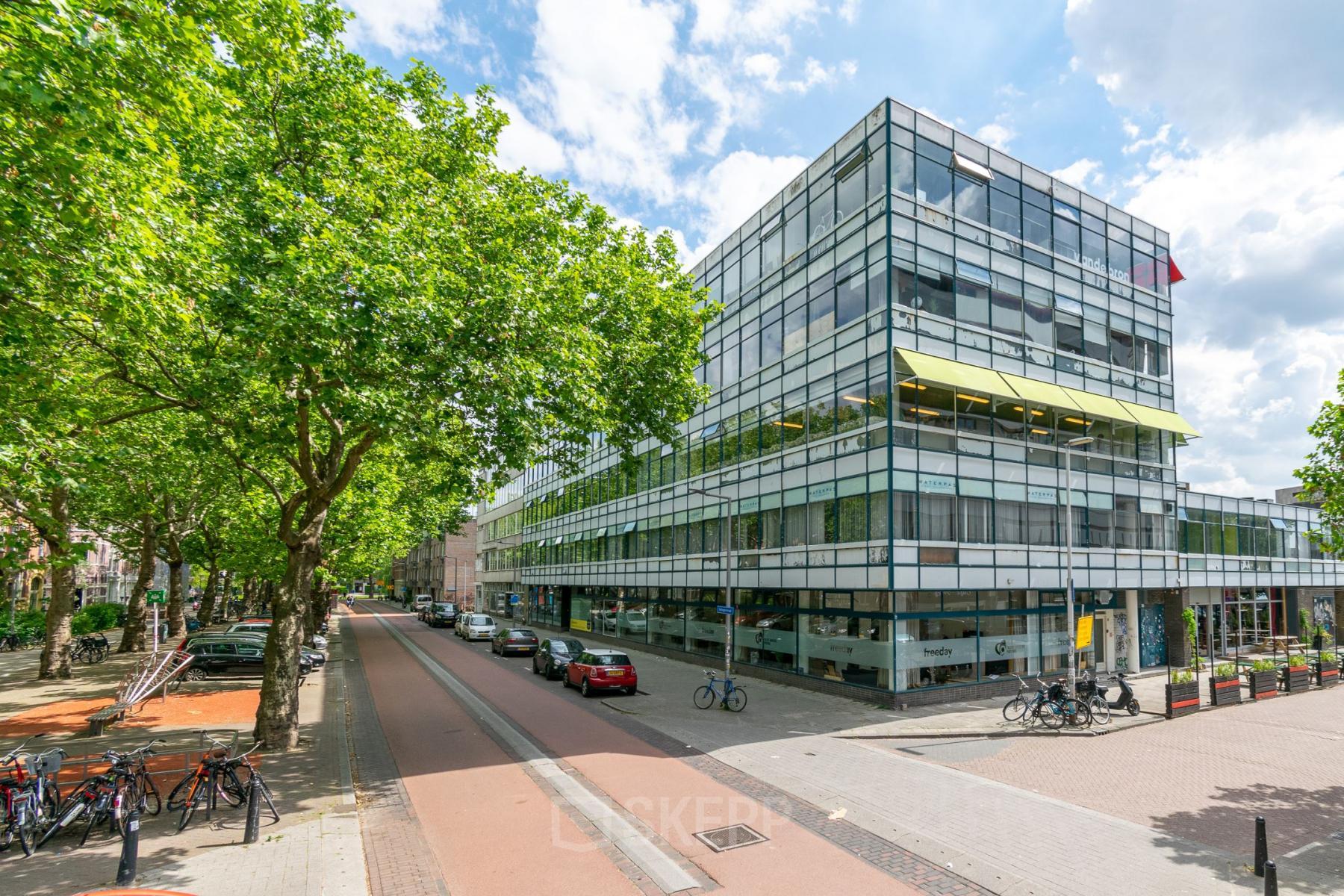 Kantoorpand aan de Vijverhofstraat 47, Rotterdam Noord. Modern gebouw met glazen gevels, omringd door bomen en geparkeerde auto's. Ideaal om een kantoorruimte te huren.