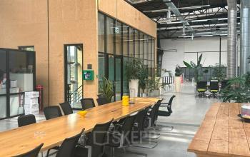 Ruime en moderne kantoorruimte huren op Scheepsbouwweg 29 in Rotterdam Waalhaven, met lange houten tafel en stijlvolle kantoorstoelen, omgeven door veel groen en glazen wanden.