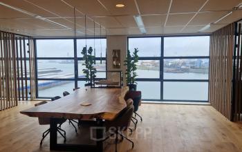 Vergaderruimte met houten tafel en stoelen, grote ramen met uitzicht op de haven, geschikt voor kantoorruimte huren in Rotterdam Waalhaven.