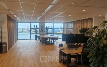 Ruime kantoorruimte met houten vloer en uitzicht op de haven. De ruimte heeft werkplekken, planten en biedt diverse zitmogelijkheden. Ideaal voor bedrijven die kantoorruimte willen huren in Rotterdam Waalhaven.
