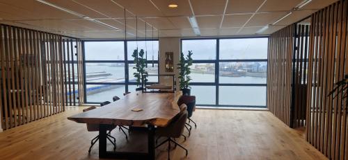 Vergaderruimte met houten tafel en stoelen, grote ramen met uitzicht op de haven, geschikt voor kantoorruimte huren in Rotterdam Waalhaven.