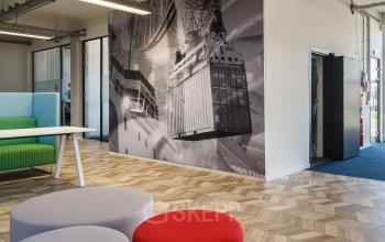 Moderne kantoorpandruimte aan Overschieseweg 34, Schiedam, met kleurrijke zitgelegenheden en een grote zwart-wit muurfoto van een containerterminal.