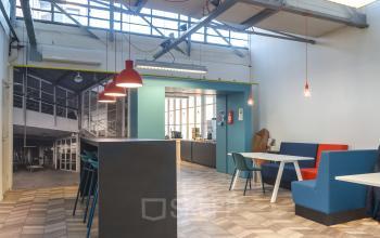 Interieur van kantoorruimte op Overschieseweg 34, Schiedam, met moderne meubels, helder verlicht en industriële uitstraling. Voorzitstoelen, tafels, en hanglampen aanwezig.