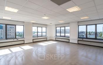 Leeg, ruim kantoor met grote ramen aan de Overschieseweg 304-332 in Schiedam, klaar voor wie kantoorruimte wil huren. Natuurlijk licht stroomt overvloedig binnen, omringd door stadsgezichten.