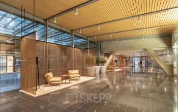 Ruime inloop bij Schiphol Boulevard 127 met moderne fauteuils, houten plafonds en veel natuurlijk licht. Ideaal om kantoorruimte te huren in een eigentijdse setting.