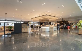 Modern kantoorpand met gemeubileerde lounge en mensen die zakelijke gesprekken voeren bij een bar op Schiphol Boulevard 127. Ideaal voor kantoorruimte huren op Schiphol Airport.