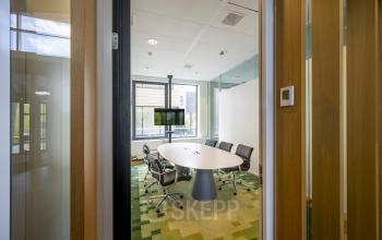 Vergaderruimte in het kantoorpand op Boeingavenue 223 – 239 in Schiphol Rijk met vijf stoelen rond een ovale tafel, grote ramen en een scherm op de achtergrond.