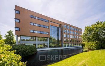 Buitenzijde van een modern kantoorpand aan Boeing Avenue 1-19 in Schiphol Rijk, omgeven door groen en een waterpartij. Ideale locatie voor kantoorruimte huren.