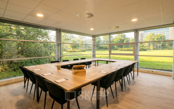 Vergaderruimte met lange houten tafel en stoelen in kantoorpand te huur op Boeing Avenue 1-19, Schiphol Rijk, met uitzicht op groene buitenruimte.