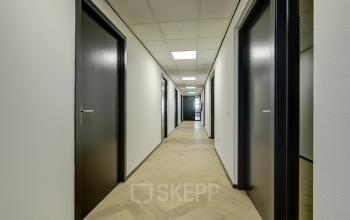 Gang met houten vloer en zwarte deuren in een kantoorpand op Fischerpad 106, Sittard, te huur als kantoorruimte.