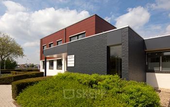 Exterieur van een kantoorpand op Nusterweg 63, Sittard, met moderne architectuur omgeven door groene heggen. Ideaal voor kantoorruimte huren met voldoende parkeerplek.