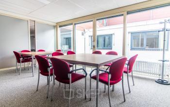 Moderne kantoorruimte in Sittard met grote ramen, rode stoelen en een ruime tafel, ideaal om in te werken of te vergaderen.