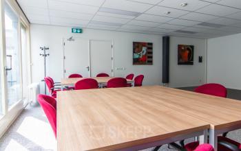 Kantoorruimte in Sittard met houten tafels en rode stoelen, ideaal om te huren voor zakelijke bijeenkomsten.