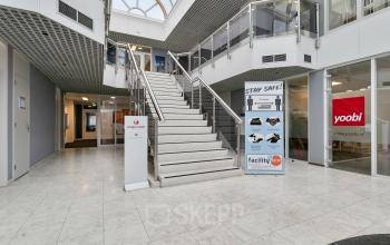 Kantoorpand aan Curieweg 7 in Spijkenisse met moderne entree en open trapopgang, ideaal voor kantoorruimte huren. De ruime, lichte omgeving biedt een warme welkom aan bezoekers en werknemers.