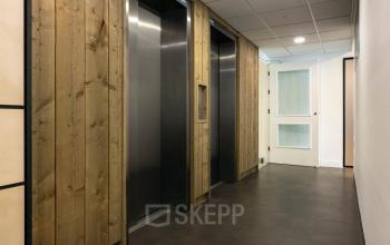 Gang met liftdeuren en houten accenten in een kantoorpand aan de Curieweg 9, Spijkenisse.