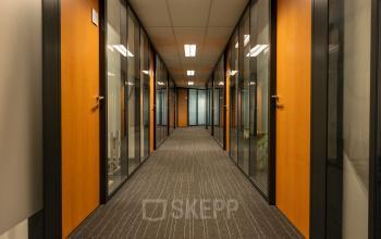 Glazen kantoorruimtes aan een centrale gang op Curieweg 9, Spijkenisse, klaar voor verhuur. De kantoorpand beschikt over houten deuren en moderne verlichtingsplafonds.