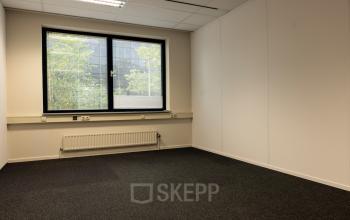 Leeg kantoor op Curieweg 9 in Spijkenisse, met grijze vloerbedekking en groot raam, ideaal voor uw kantoorruimte huren.
