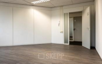 Lege kantoorruimte met houten vloer en glazen deur op Curieweg 9, Spijkenisse. Geschikt voor het huren van een veelzijdige werkplek.