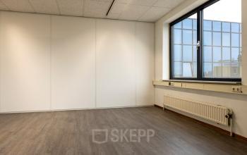 Een lichte kantoorruimte met houten vloer en groot raam aan de Curieweg 9 in Spijkenisse, ideaal voor kantoorruimte huren.