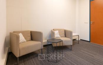 Stijlvolle kantoorruimte huren op Curieweg 9 in Spijkenisse met moderne, minimalistische inrichting, voorzien van twee comfortabele fauteuils, een bijzettafel en kussenaccenten.