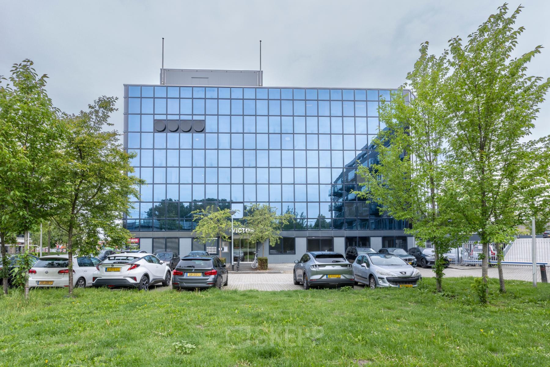 Vooraanzicht van een modern kantoorpand gelegen aan de Curieweg 9, Spijkenisse, met een glazen gevel en parkeerruimte. Ideaal voor wie kantoorruimte wil huren in een strak en professioneel gebouw.