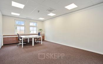 Ruime kantoorruimte op Bredaseweg 8, Breda Terheijden, met strakke muren, donker tapijt en een groot bureau met stoelen, perfect om te huren voor zakelijke activiteiten.