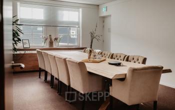 Kantoorruimte huren aan Bredaseweg 8, Breda Terheijden. Ruime vergaderruimte met lange tafel en comfortabele stoelen, geschikt voor zakelijke bijeenkomsten. Grote ramen voor natuurlijke lichtinval.