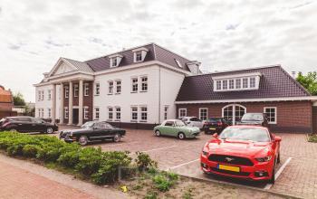 Kantoorpand aan Bredaseweg 8, Breda Terheijden met meerdere geparkeerde auto's waarvan een opvallende rode sportwagen. Ideaal voor bedrijven die kantoorruimte willen huren in deze charmante omgeving.
