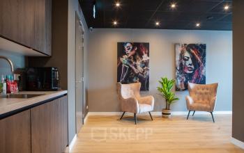 Kantoorruimte met moderne inrichting aan de Kapitein Rondairestraat 8 in Tilburg, voorzien van comfortabele fauteuils, kunst aan de muur en een klein keukenblok. Ideaal om een kantoor te huren.