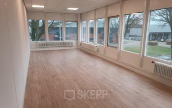 Goed verlichte kantoorruimte te huur op Jules de Beerstraat 14, Tilburg, met grote ramen die uitzicht bieden op een groene buitenruimte.