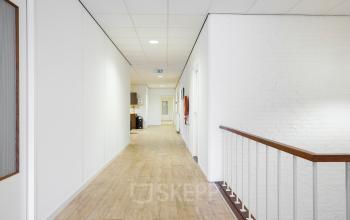 Gang bij kantoorruimte huren in kantoorpand op Jules de Beerstraat 14, Tilburg, met houten vloer en witte muren.