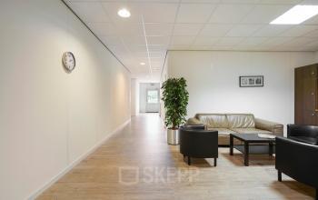 Kantoorruimte huren aan de Jules de Beerstraat 14, Tilburg. Ruime gang met banken en stoelen, houten vloer, kamerplanten en muurdecoratie.