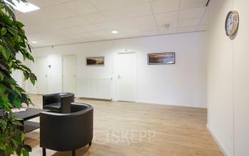 Stijlvolle kantoorruimte huren op Jules de Beerstraat 14 in Tilburg, met modern interieur, twee zwarte stoelen, kunst aan de muur en een klok.