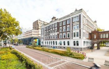Klassiek vier verdiepingen hoog kantoorpand aan Moreelsepark 1, Utrecht Centraal Station, met bakstenen en witte accenten, omgeven door groene plantsoenen en stedelijke architectuur.