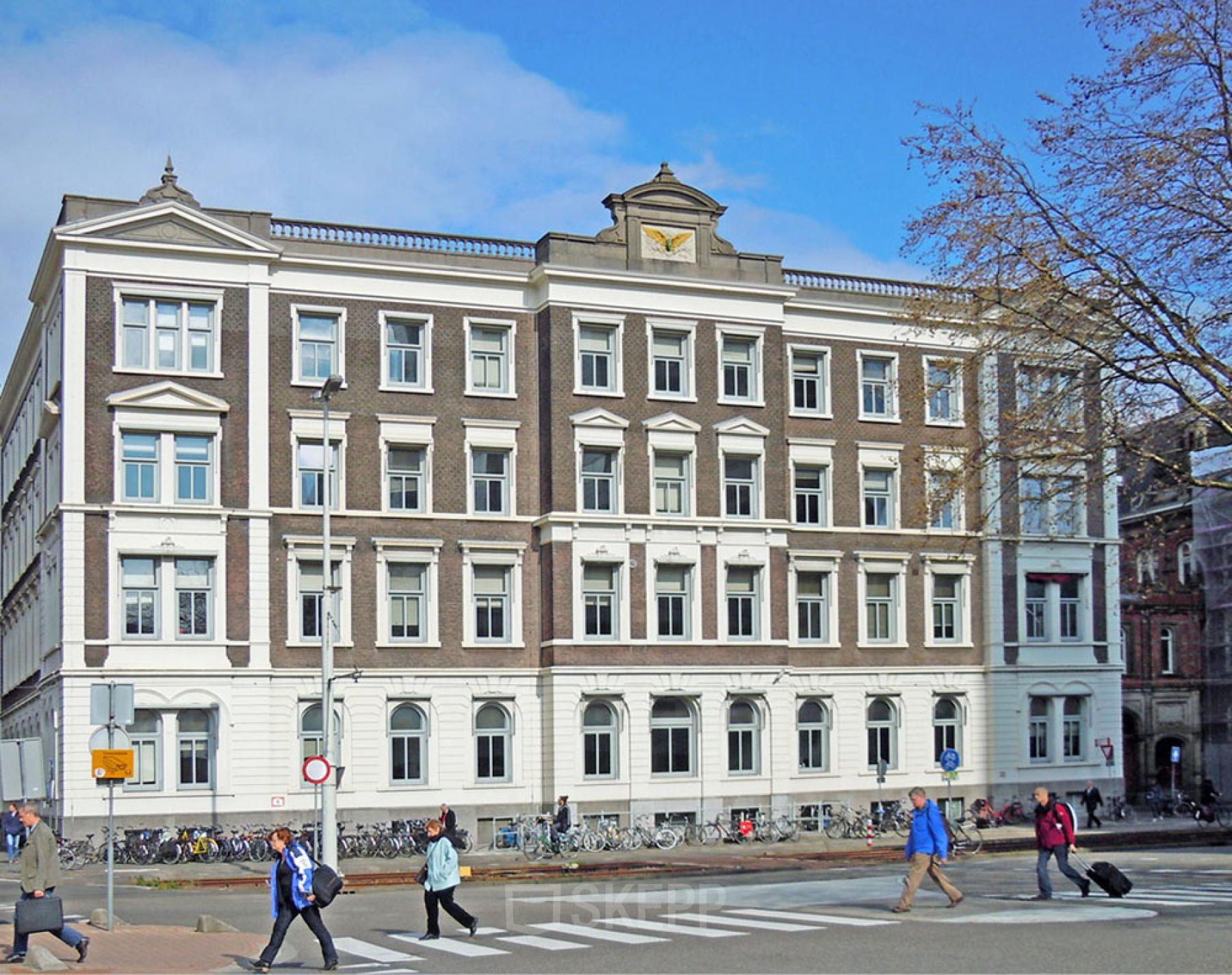 Het kantoorpand aan Moreelsepark 1, Utrecht Centraal Station, biedt een klassieke uitstraling. Mensen lopen langs de historische gevel richting hun bestemming.