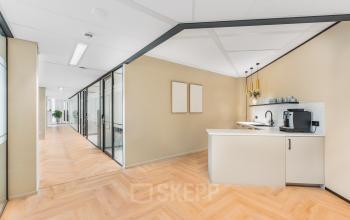 Moderne kantoorruimte met glazen wanden en een compacte pantry in een kantoorpand bij Utrecht Centraal Station. Geschikt voor huur, met lichte houten vloer en stijlvolle inrichting.